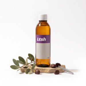 Botella ámbar de 1 litro de Aceite de Jojoba Golden Virgen de LTSH, con hojas y semillas de jojoba sobre piedra